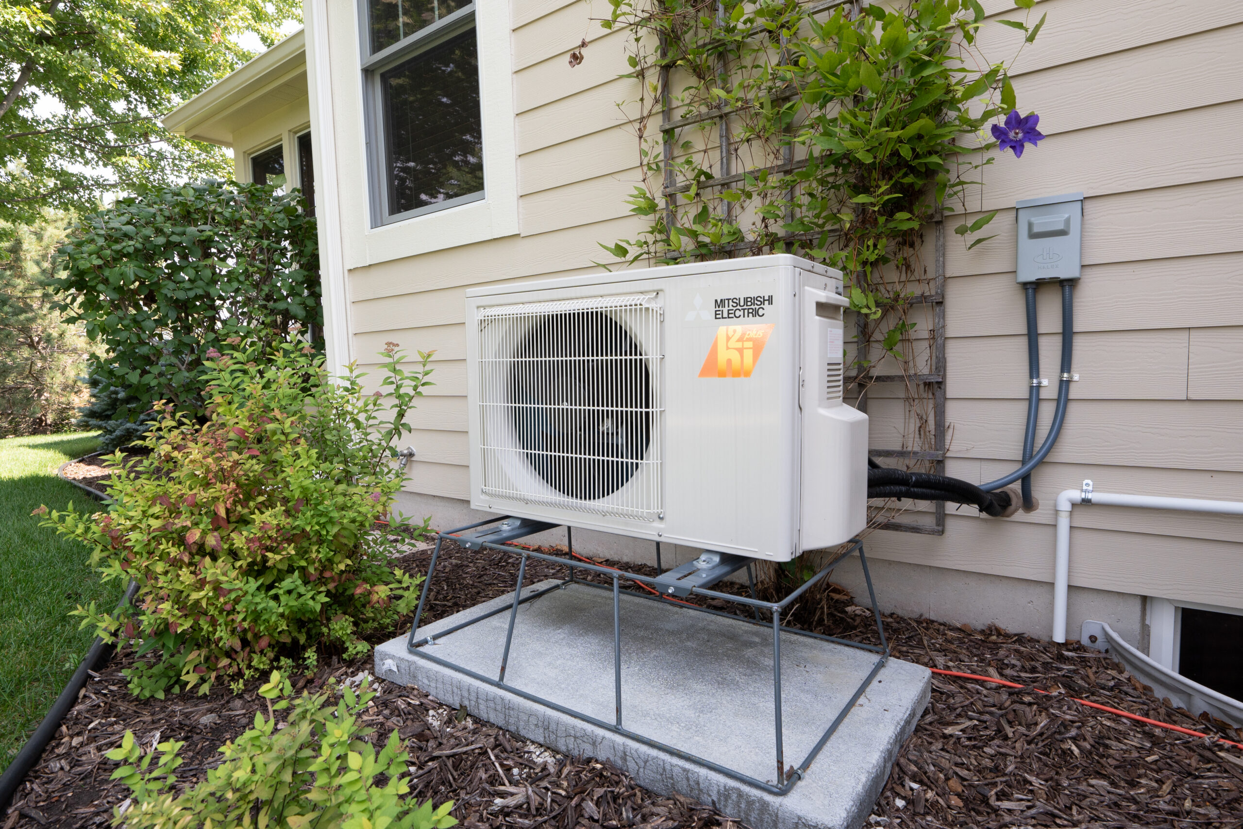 Mitsubishi Electric outdoor heat pump mounted on an elevated stand beside a home